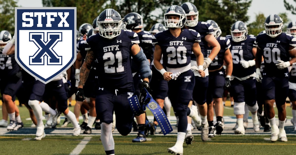 StFX football players in navy run onto the field together, with the StFX crest in the corner