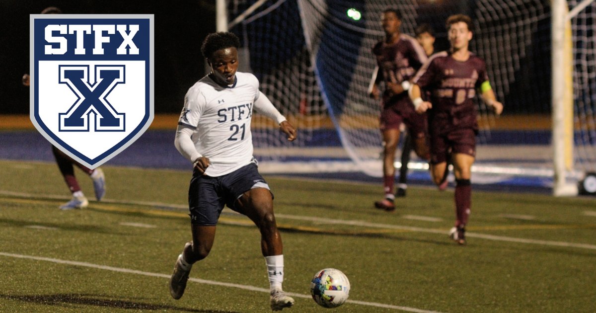 A StFX men's soccer player in white dribbles under the lights with the goal behind him, with the StFX crest in the corner