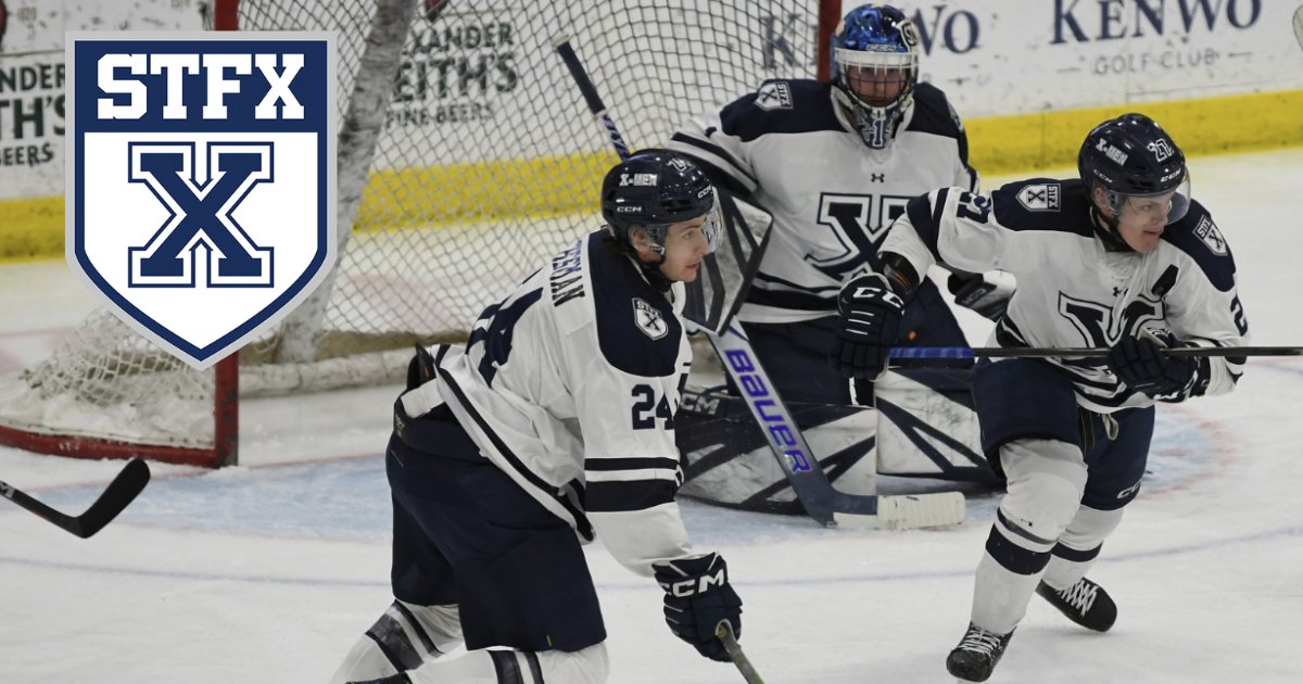Two StFX men's hockey players in white skate in front of their goaltender, with the StFX crest in the corner